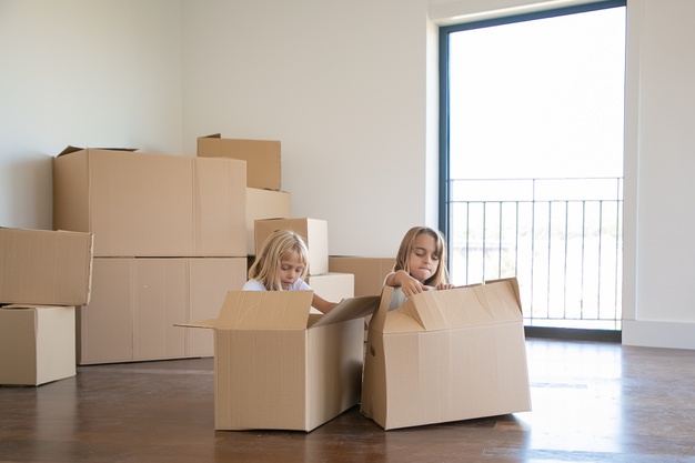 two-adorable-girls-unpacking-things-new-apartment-sitting-floor-near-open-cartoon-boxes_74855-10436